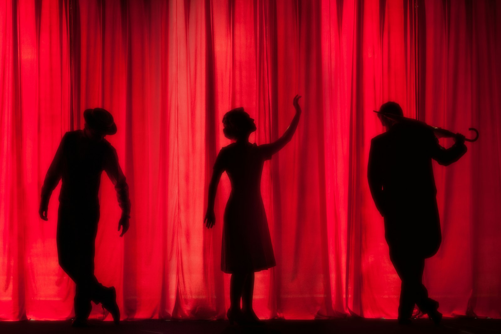 Silhouettes de comédiens devant un rideau de scène rouge